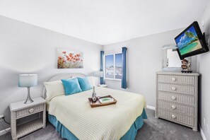 A bedroom with a bed, bedside tables, a dresser, a television, and a window with curtains. - Breezy Condo | Deluxe Pool & Private Beach Access (Marco Island)