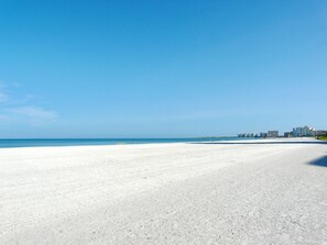 A wide, sandy beach with a clear blue sky and calm sea.