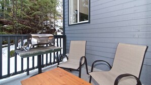 A patio with a wooden table and two chairs, a grill, and a railing. - Charming Creekside Townhouse. Easy WALK to the Gondola. Professionally Managed + Cleaned (Whistler)