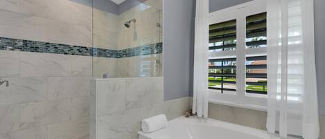 Un baño moderno con cabina de ducha de vidrio, una bañera grande y una ventana con persianas.