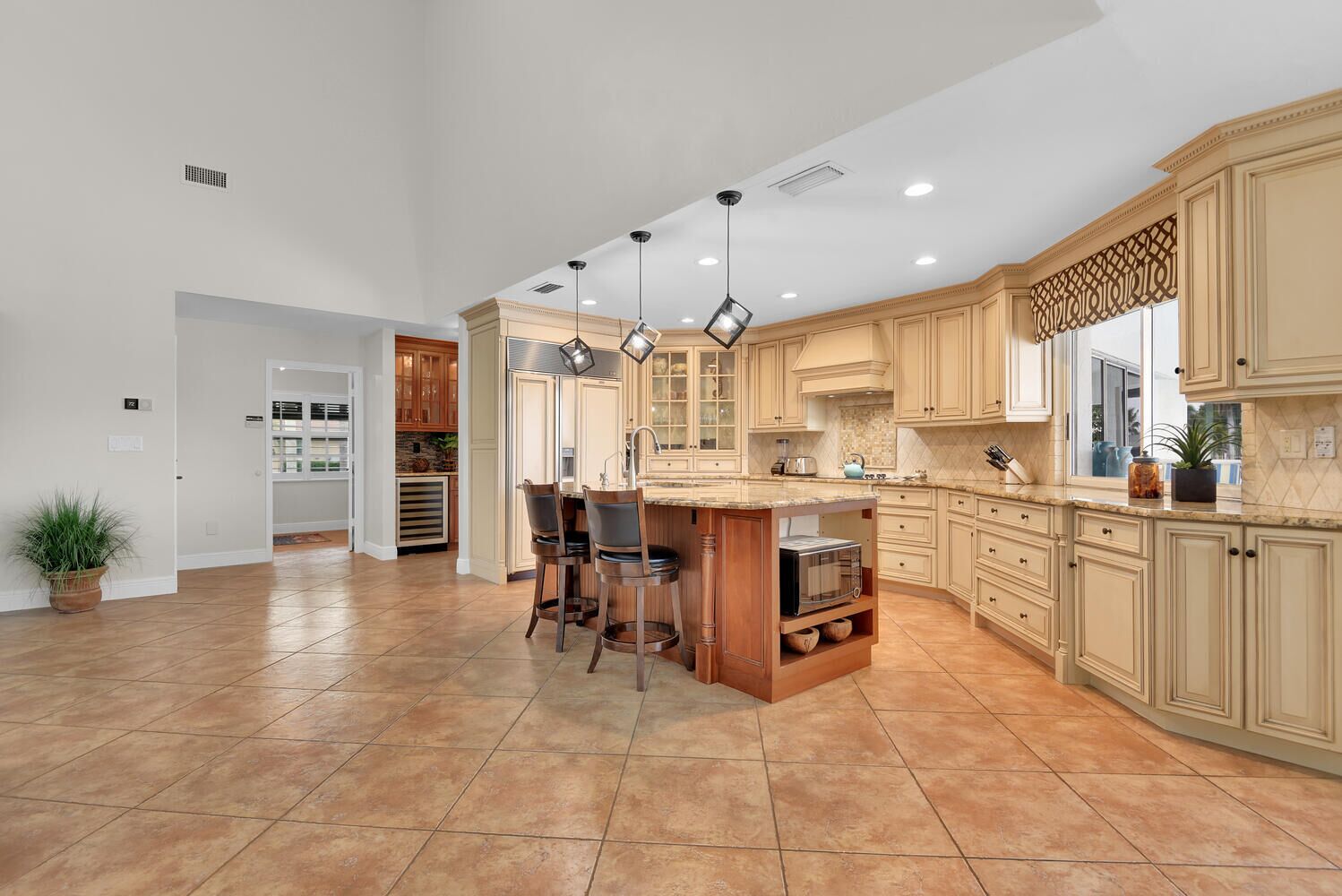 A spacious kitchen with a large island, wooden cabinets, and a tiled floor.