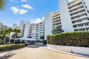 A modern hotel with multiple floors, a paved courtyard, and a well-maintained garden with palm trees and hedges.