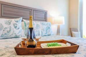 A wooden tray on a bed with a bottle of Brut Cuvée wine and two glasses, a plate of grapes, and a floral-patterned bedspread.