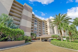 A multi-story hotel with a central courtyard, palm trees, and a clear blue sky.