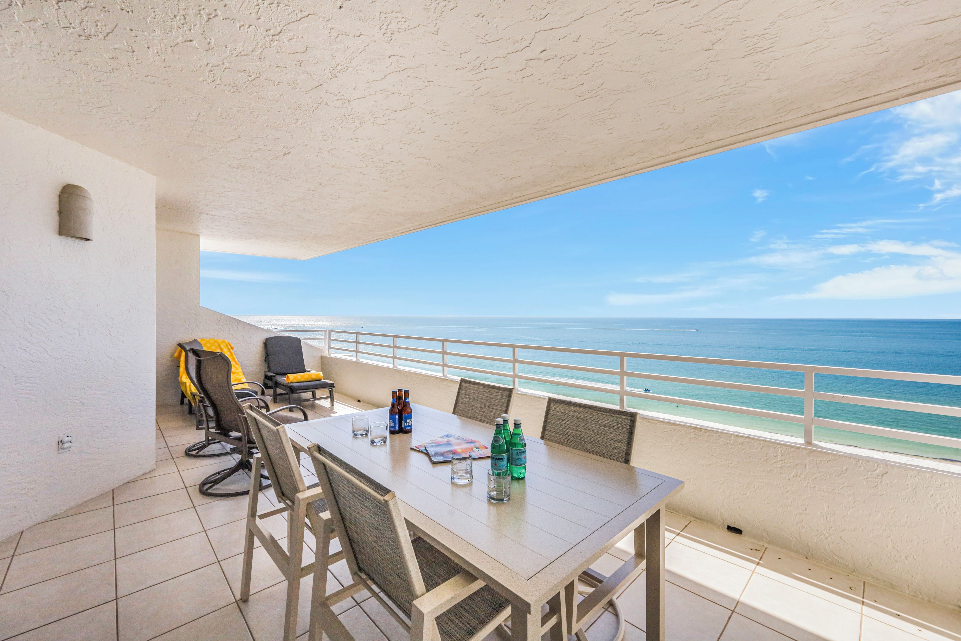 Een balkon met een tafel en stoelen, met uitzicht op een strand.