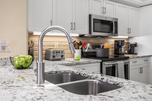A modern kitchen with white cabinets, a stainless steel sink, a microwave, and a toaster. - Beachfront Condo | Huge Views/Pools/Tennis/Grills (Marco Island)