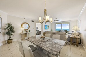 A spacious living area with a marble dining table, comfortable seating, a ceiling fan, and a view of the ocean. - Beachfront Condo | Huge Views/Pools/Tennis/Grills (Marco Island)