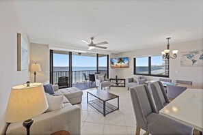 A spacious living area with a balcony overlooking the sea, furnished with sofas, a coffee table, and a TV. - Inviting Beachfront Condo | Pool, Spa & Views (Marco Island)