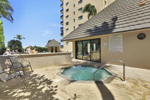 A hot tub area with a 'NO DIVING' sign, surrounded by lounge chairs and a building with a tiled roof. - Inviting Beachfront Condo | Pool, Spa & Views (Marco Island)