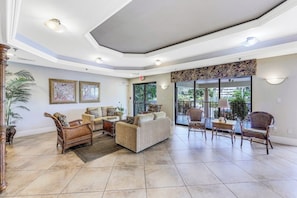 A spacious lobby with a high ceiling, a large seating area with sofas and chairs, a large window with a view of greenery, and a patterned wall decoration. - Inviting Beachfront Condo | Pool, Spa & Views (Marco Island)