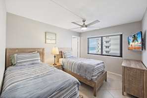 A bedroom with two beds, a ceiling fan, a window with blinds, and a painting on the wall.