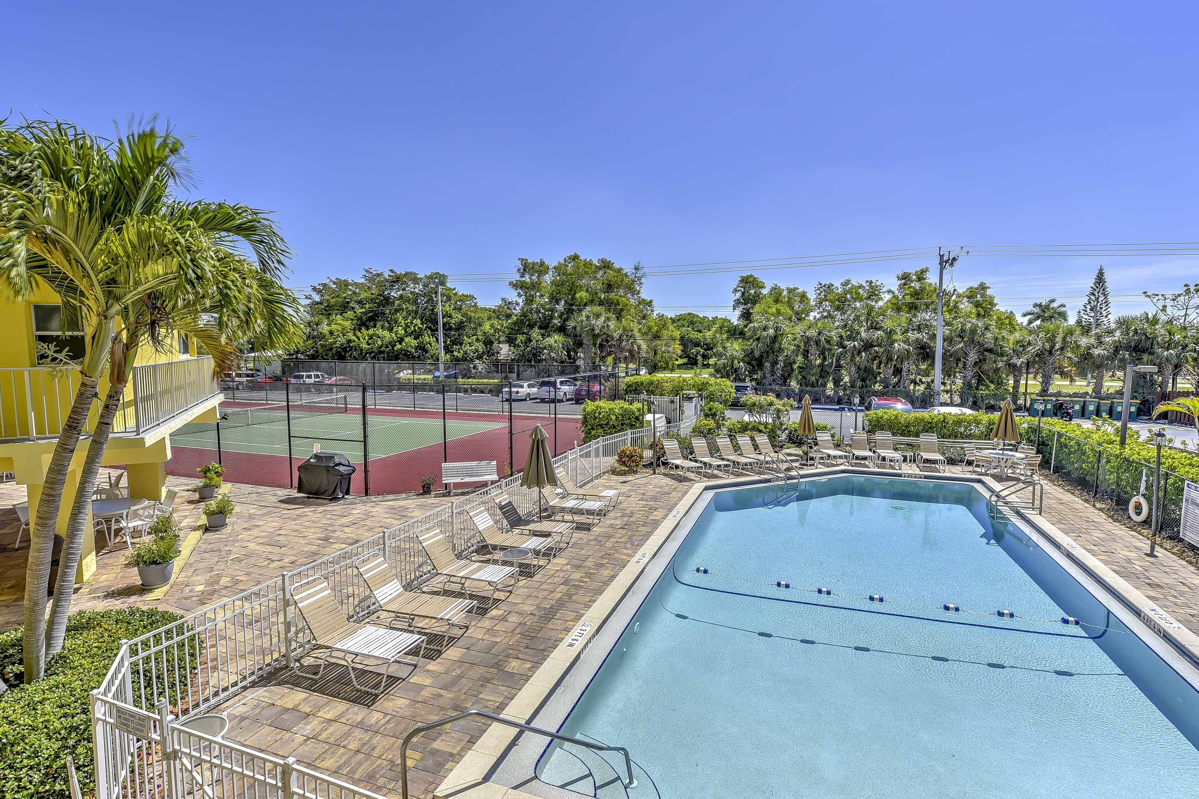 Una piscina con lettini e un campo da tennis sullo sfondo.