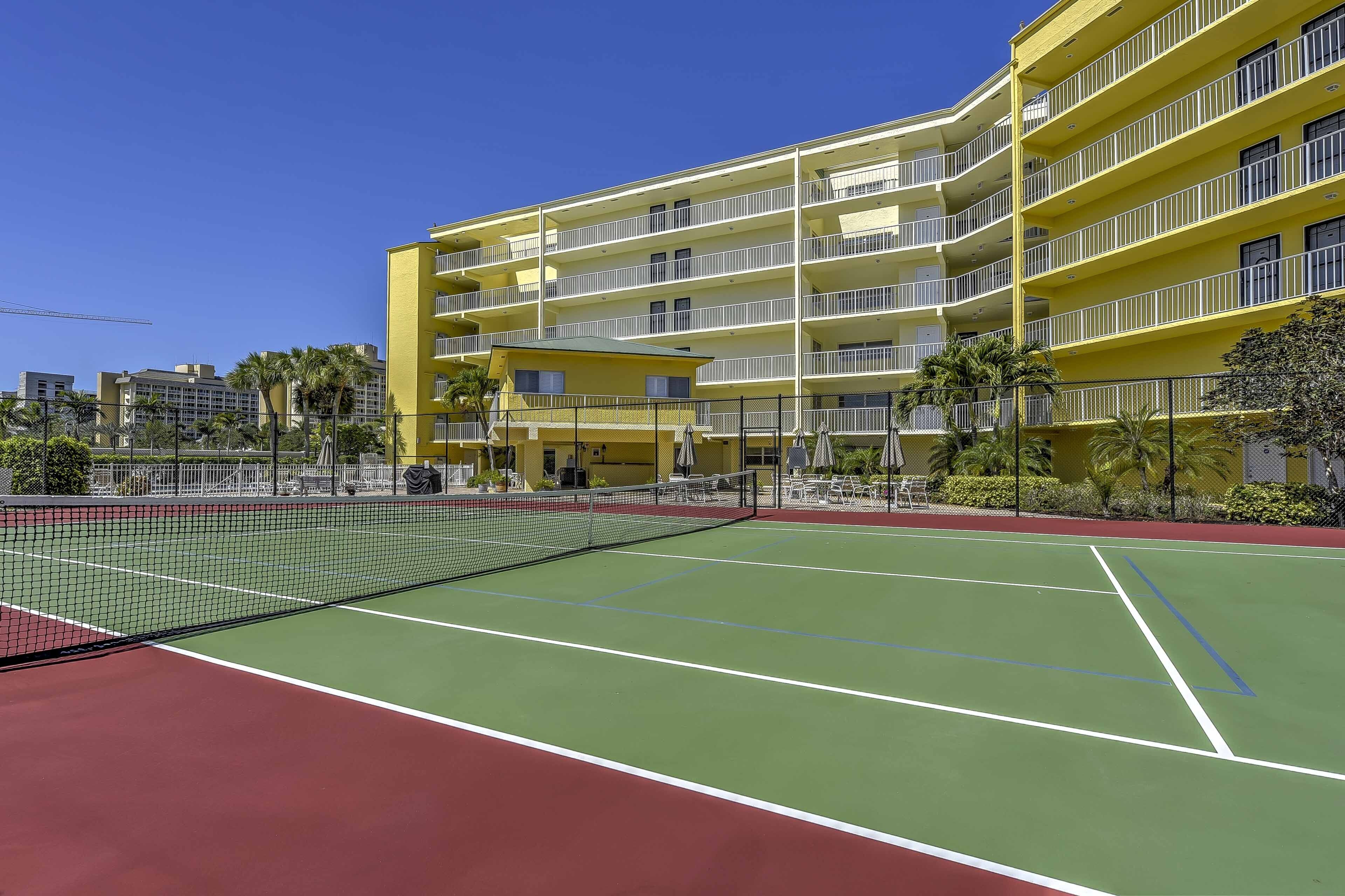 Een tennisbaan met een net in het midden, omringd door een geel gebouw met balkons.