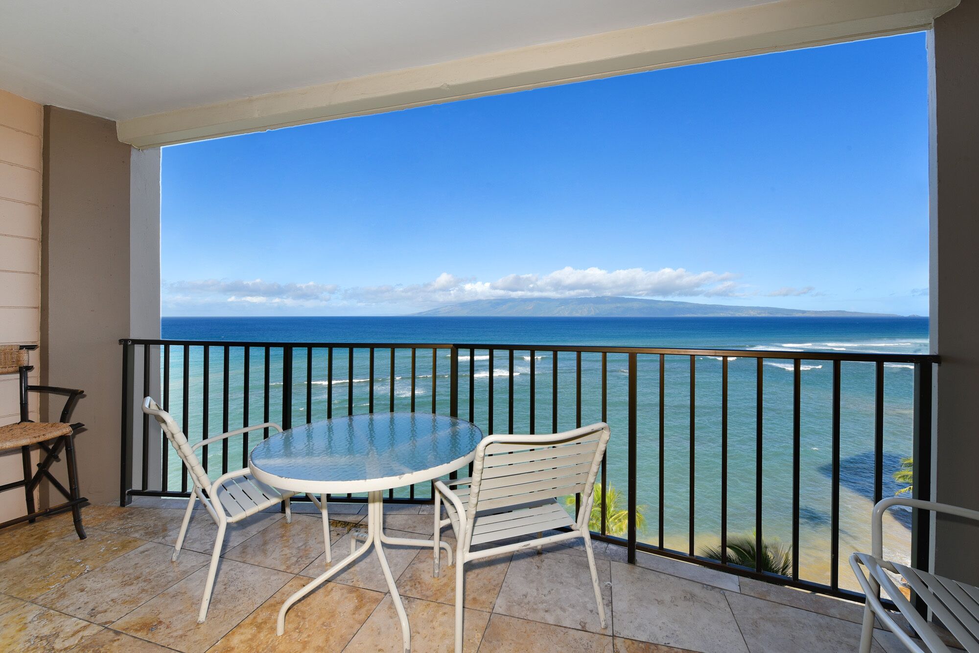 Ein Balkon mit Glastisch und Stühlen, der auf einen Strand und den Ozean blickt.