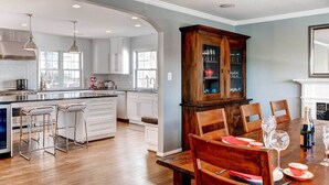 A spacious kitchen with white cabinets, a wooden dining table set for six, and a large wooden cabinet with glass doors. - Southern-Style Home w/ Luxe Kitchen: 15 Min to DC! (Arlington)