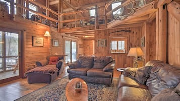 A cozy log cabin interior with a leather sofa, ottoman, and a large rug.