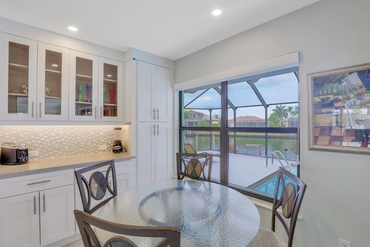 A modern kitchen with white cabinets, a glass-top dining table, and a view of a pool and outdoor area.