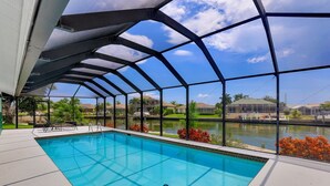 Ein Schwimmbad mit Glasüberdachung, umgeben von einer Terrasse und Blick auf einen See und Häuser.