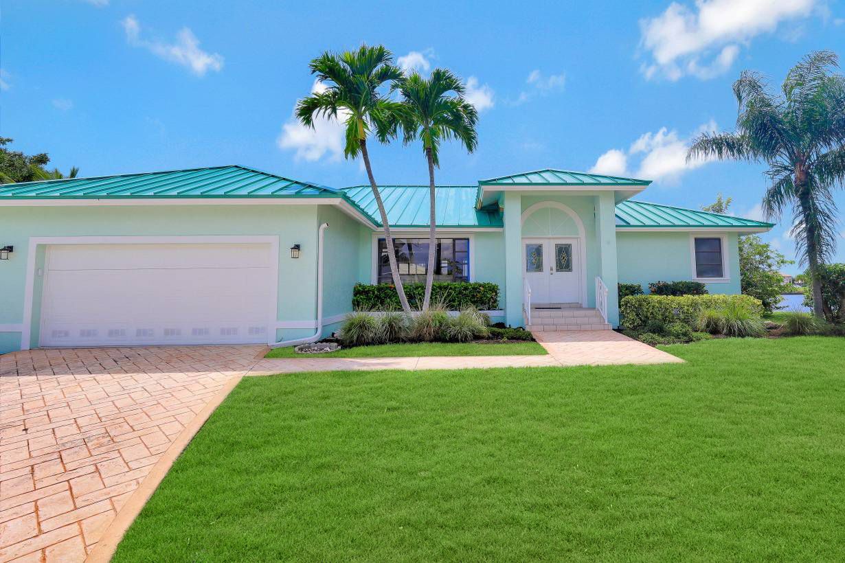 A two-story house with a green roof, a garage, and a well-maintained lawn.