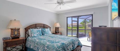 A bedroom with a bed, two bedside tables with lamps, a ceiling fan, and a view of the outdoors through a sliding glass door.