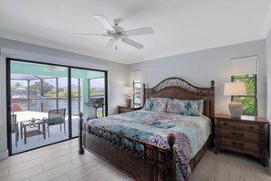 A spacious bedroom with a large bed, a ceiling fan, and a view through a sliding glass door to an outdoor patio area. - Pet-Friendly Waterfront Home | Key Lot w/ View (Marco Island)