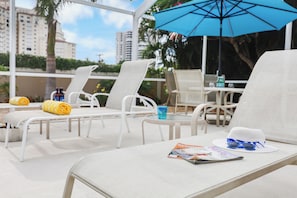 Zona de piscina con sillones reclinables, una mesa y una revista.