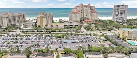 A coastal hotel area with multiple buildings, a parking lot, and a beach in the background.