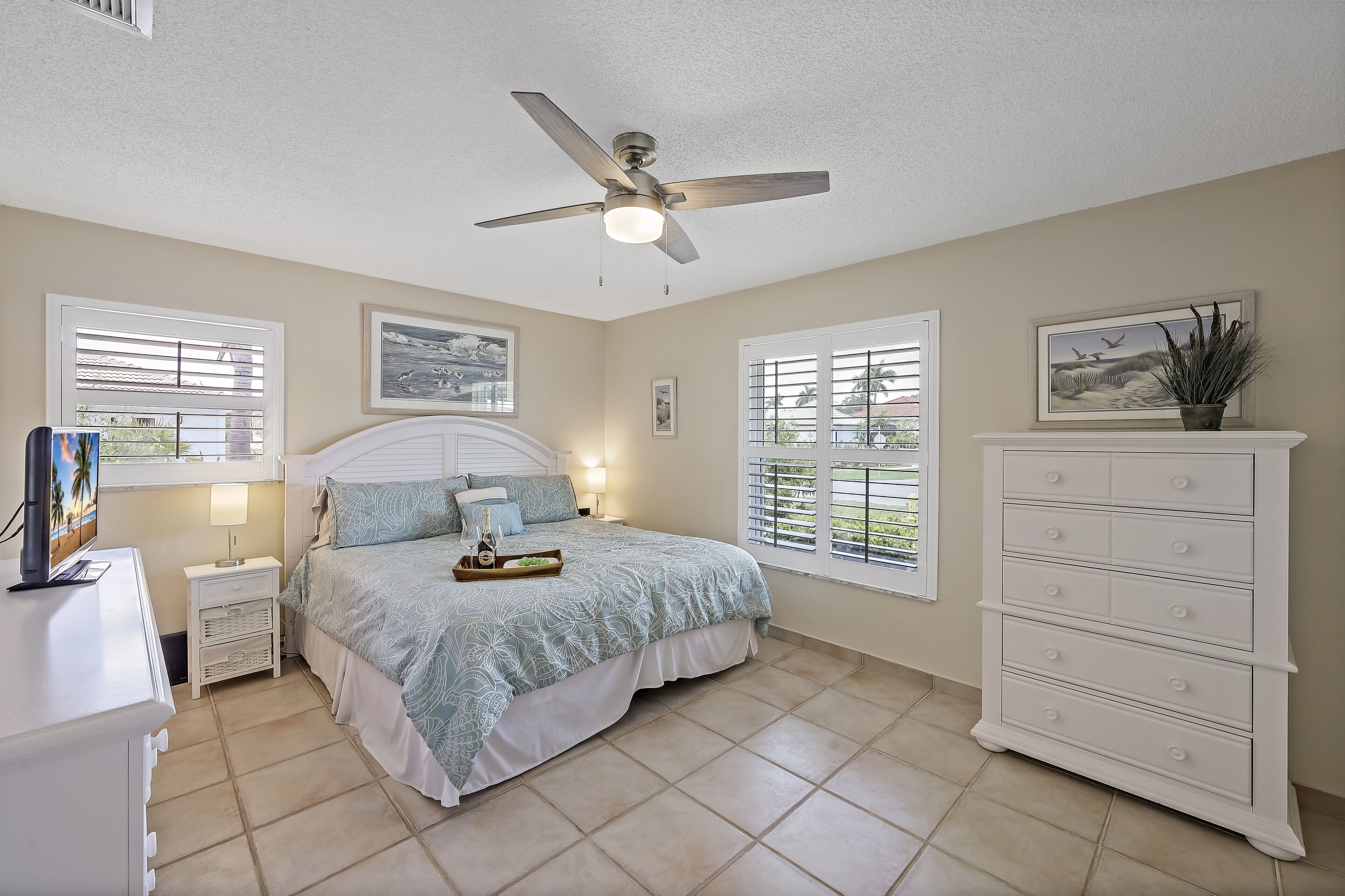 A bedroom with a bed, nightstands, a dresser, a ceiling fan, and windows with blinds.