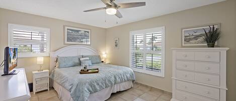 A bedroom with a bed, nightstands, a dresser, a ceiling fan, and windows with blinds.
