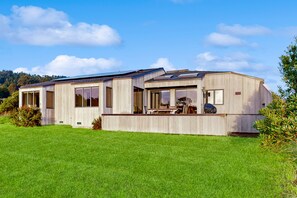 Enjoy a spacious living area with large windows, a patio, and covered outdoor seating area, surrounded by a well-maintained lawn and rolling hills.
