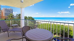 A balcony with wicker furniture, a round table, and a view of the beach and ocean. - Luxurious Beachfront Condo | Glorious Ocean Views (Marco Island)
