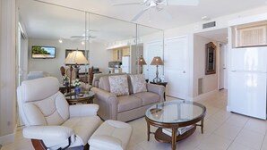 A modern living room with a sofa, armchairs, a glass coffee table, and a ceiling fan. - Luxurious Beachfront Condo | Glorious Ocean Views (Marco Island)