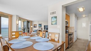 Een ruime eetruimte met een houten tafel gedekt voor zes personen, een keuken met moderne apparatuur en uitzicht op de oceaan door grote ramen.