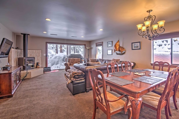 A spacious living area with a large wooden dining table, comfortable seating, a fireplace, and large windows offering a view of the outdoors. - Private Deck & Community Pool: Incline Village Gem (Incline Village)
