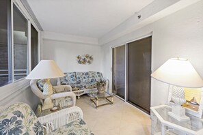 Ein Wohnzimmer mit einer Couch, zwei Lampen, einem Glastisch und einer Schiebetür.