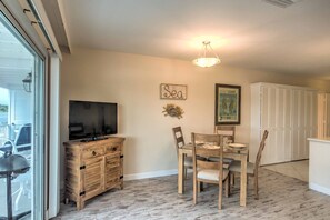 A dining area with a table and chairs, a television on a wooden cabinet, and a ceiling light fixture. - Waterfront Sunset Suite: Dolphins, Docks & Pool! (Marco Island)