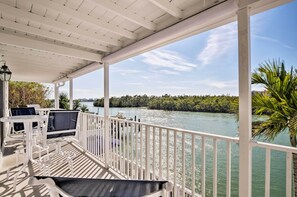 Una terrazza esterna coperta con ringhiere bianche, posti a sedere e vista su un fiume e del verde.