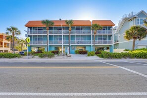 Et hotel ved stranden med flere balkoner, palmer og en klar himmel.