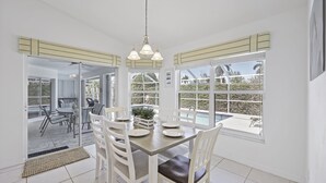 A dining area with a table set for four, white chairs, and a view of the outdoors through large windows. - Inviting and Quiet Home | Pool & Steps to Beach (Marco Island)