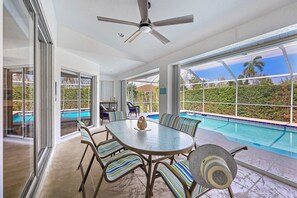 A spacious indoor area with a pool, a ceiling fan, and a table with striped chairs. - Inviting and Quiet Home | Pool & Steps to Beach (Marco Island)
