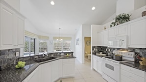 A modern kitchen with white cabinets, granite countertops, and a large island. - Inviting and Quiet Home | Pool & Steps to Beach (Marco Island)
