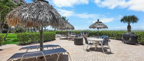 A patio area with lounge chairs, a thatched umbrella, and a view of the ocean.