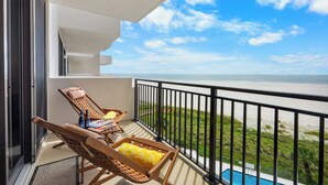 Un balcon avec deux fauteuils de jardin en bois, une piscine et une vue sur la plage.