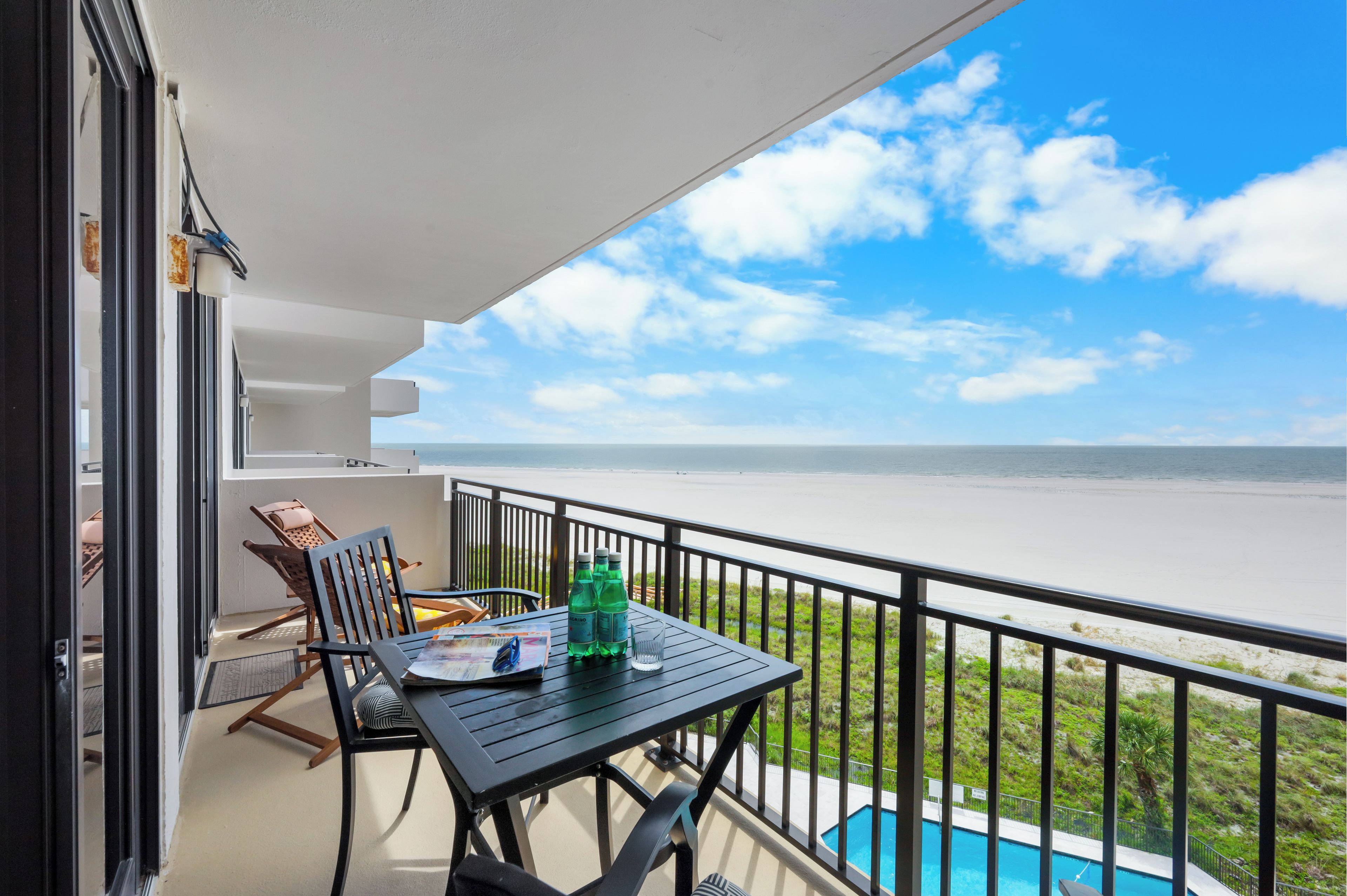 A balcony with a table, chairs, and a view of the beach and ocean.