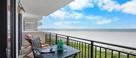 A balcony with a table, chairs, and a view of the beach and ocean.