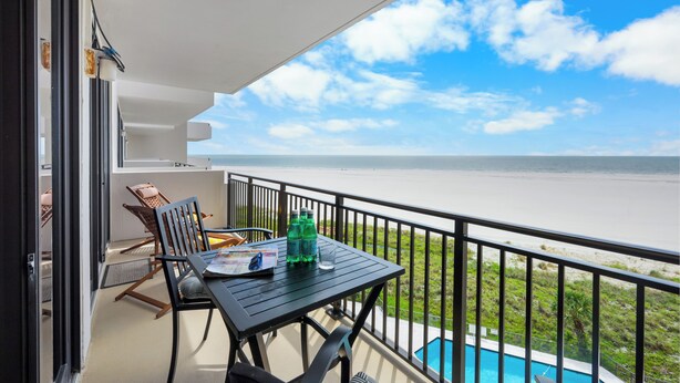 Un balcon avec une table, des chaises et une vue sur la plage et l’océan.