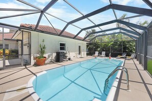 An indoor swimming pool with a glass ceiling, surrounded by lounge chairs and potted plants.