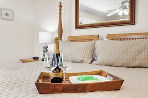 A bed with a wooden headboard, a bedside table with a lamp, and a tray with a bottle of champagne, two glasses, and green grapes.