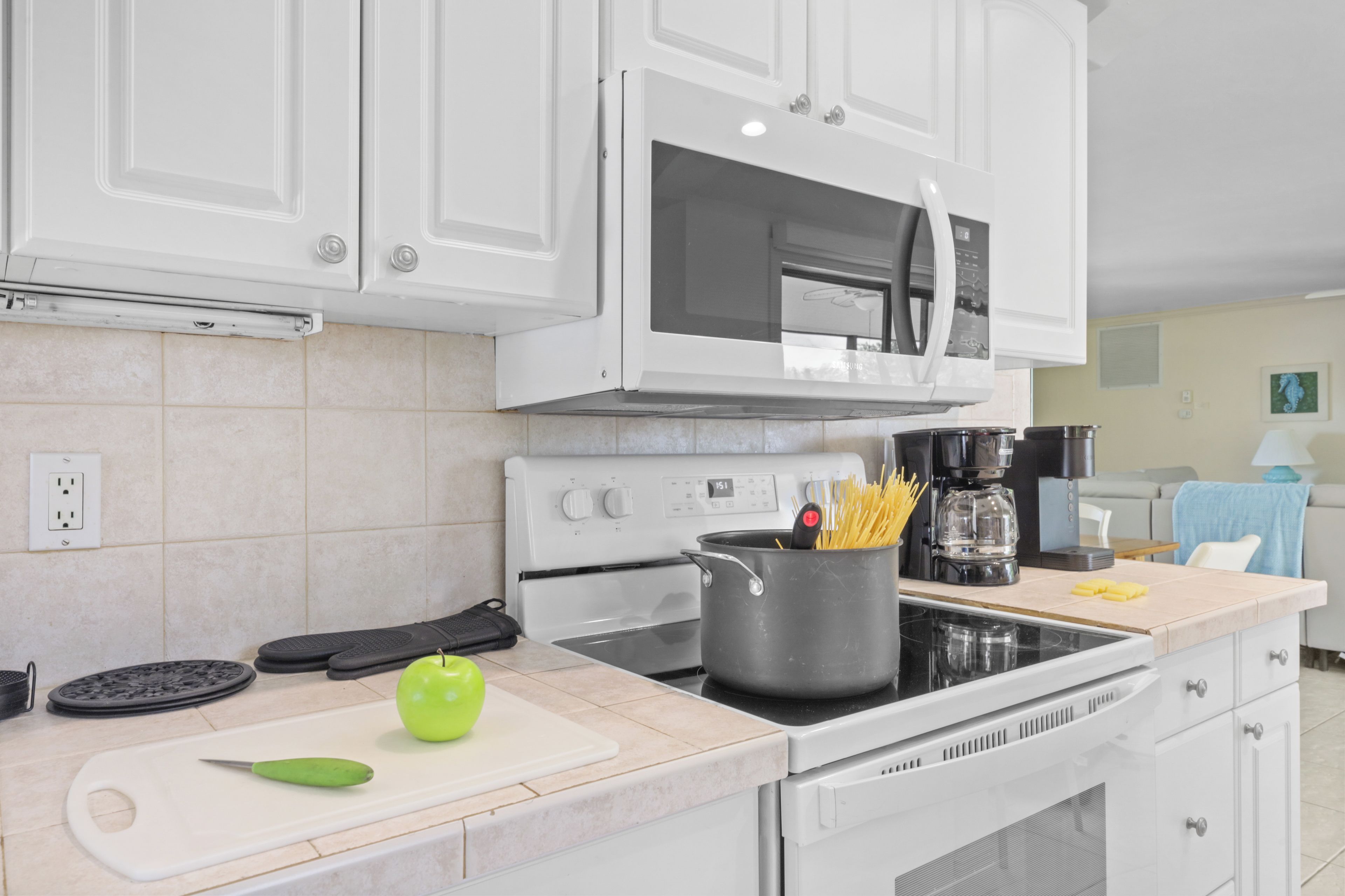 A modern kitchen with white cabinets, a stove, a microwave, and a pot of spaghetti on the counter.