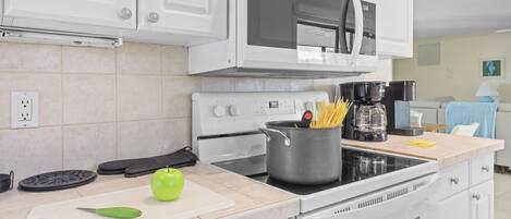 Una cocina moderna con armarios blancos, una estufa, un microondas y una olla de espagueti sobre la encimera.